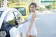 A woman in a white dress standing next to a white car.