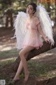 A woman in a pink dress with white wings sitting on a tree branch.