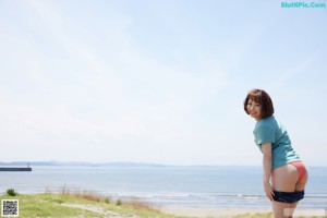 A woman in a blue shirt and red panties standing on a beach.