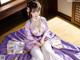 A woman in a purple and white kimono sitting on a bed.