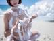 A woman in a white lingerie sitting on a beach.