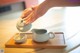 A person pouring tea into a white teapot on a wooden tray.