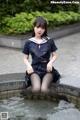 A woman in a school uniform sitting on a fountain.