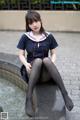 A woman in a school uniform sitting on a fountain.