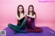 Two young women sitting on a purple yoga mat.