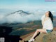 A woman sitting on top of a mountain looking out over the clouds.