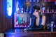 A woman sitting at a bar in front of a neon sign.